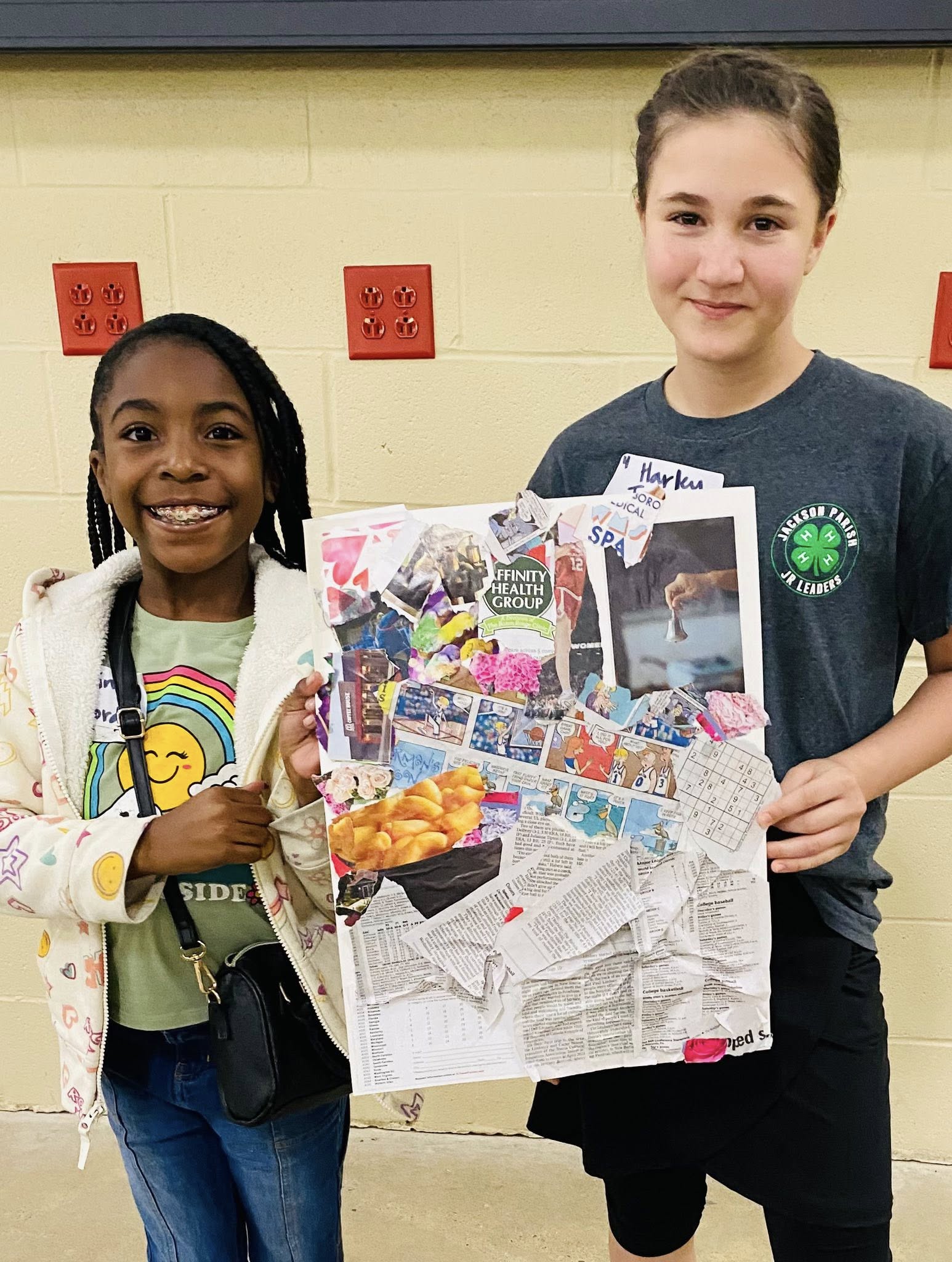 A girl and a boy holding a picture and newspaper collage.